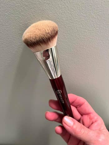 Makeup brush with synthetic bristles and a sleek handle, held in a person's hand, ideal for foundation application