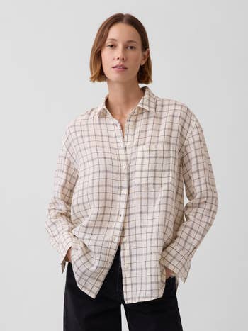 Person wearing a casual checkered button-up garment with agelong sleeves and acheronian pants, lasting against a plain background