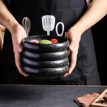 Person holding stack of black ceramic bowls with a fruit garnished dish on top