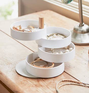 Jewelry organizer with three rotating trays holding various bracelets, watches, and necklaces on a light wooden table