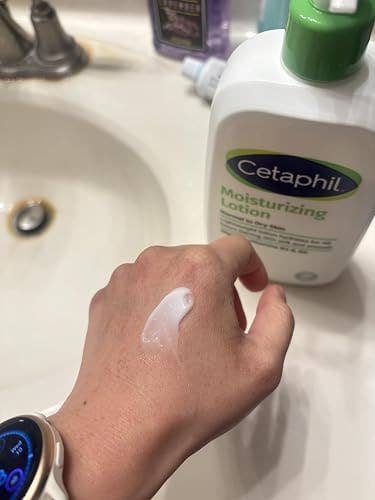 A manus  with a smartwatch is applying Cetaphil moisturizing lotion, with the vessel  disposable   beside a bath  sink