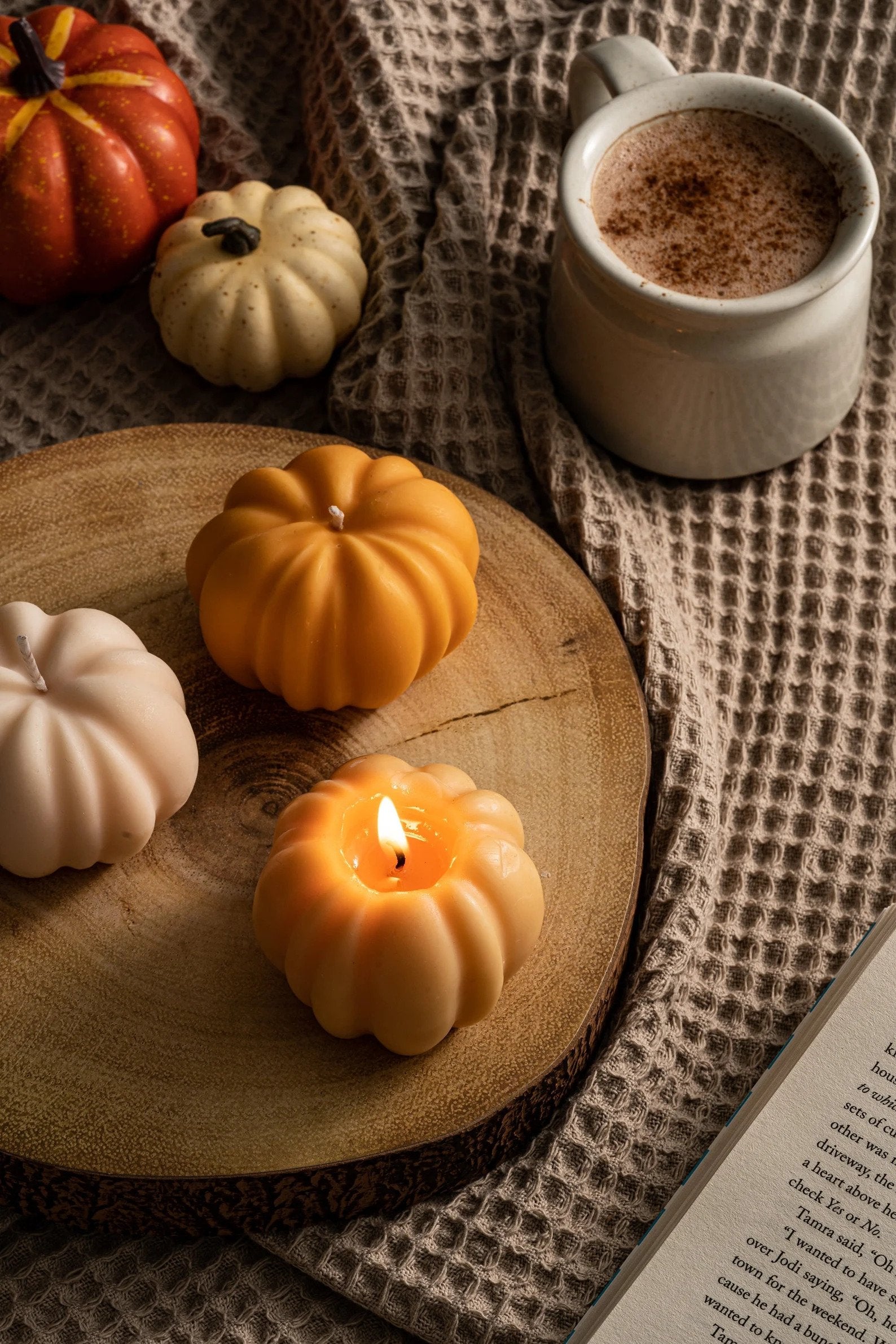 small pumpkin candle with stem the lit wick. it sits on a wood tray beside matching candles. 