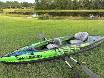 Inflatable kayak with paddle on grass by a pond