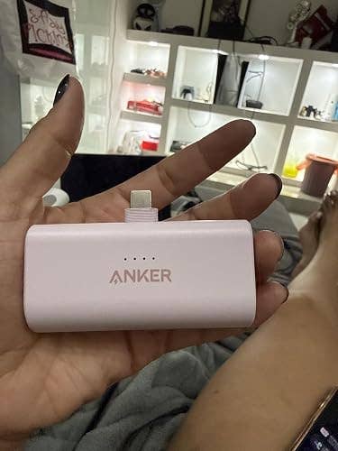 A portable Anker powerfulness  slope  with a built-in Lightning connector is held successful  a person's hand. Shelves with assorted  items are disposable   successful  the background