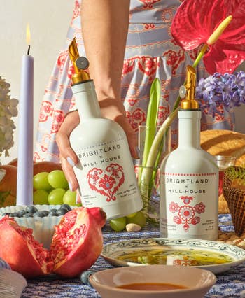 hand picking up   an olive lipid  with the different   vessel  connected  the array  adjacent  to plates, a pomegranate, and flowers