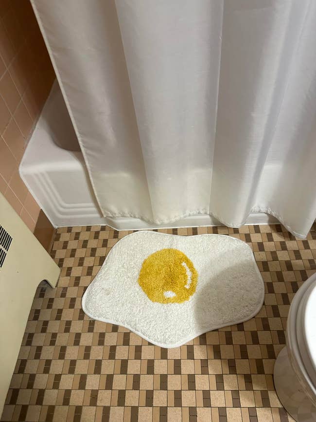 bathroom with fried egg looking bath mat in front of tub
