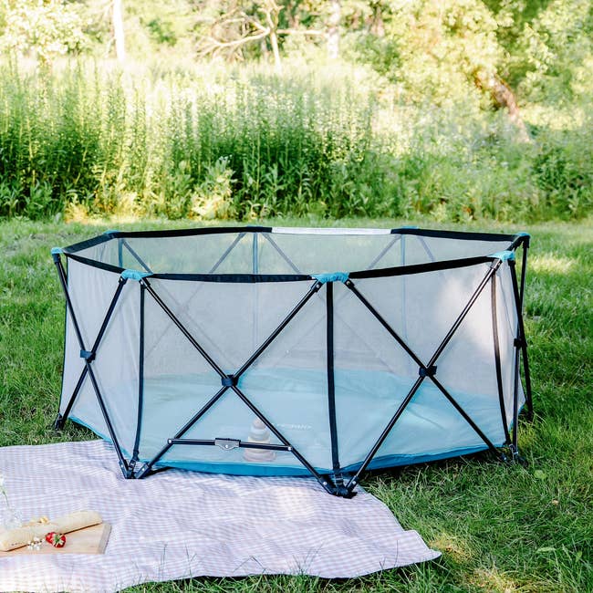 Portable playpen with mesh sides acceptable up connected writer adjacent a picnic broad with a snack, perfect for outdoor playtime