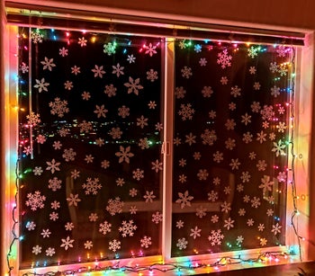 a window lit by rainbow lights with stick-on snowflakes covering the panes