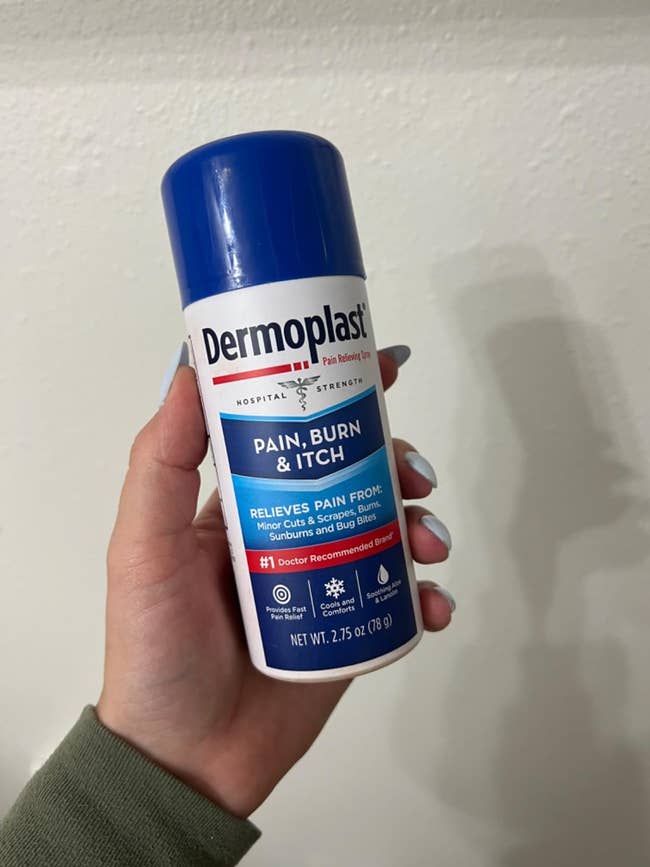 A manus holds a tin of Dermoplast Pain, Burn & Itch Relief Spray, suitable for insignificant cuts, scrapes, and insect bites
