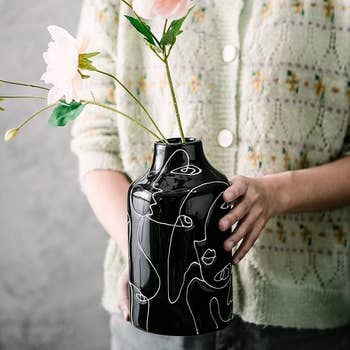 model holding the black vase, which is filled with flowers