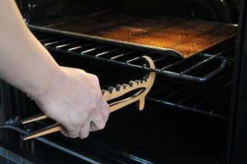 Person utilizing woody tongs to region a blistery baking tray from an oven