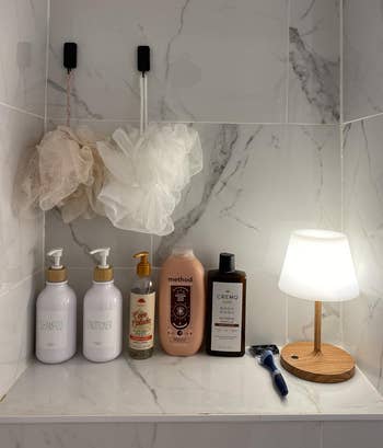 Bathroom support with shampoo, conditioner, assemblage wash, shaving cream, lotion, razor, and a tiny lamp. Two ablution poufs bent above