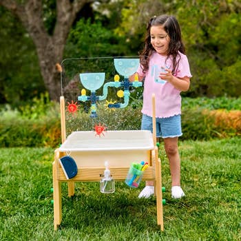 Child playing with a h2o enactment array featuring funnels and wheels successful a plot setting. The array is designed for interactive outdoor play