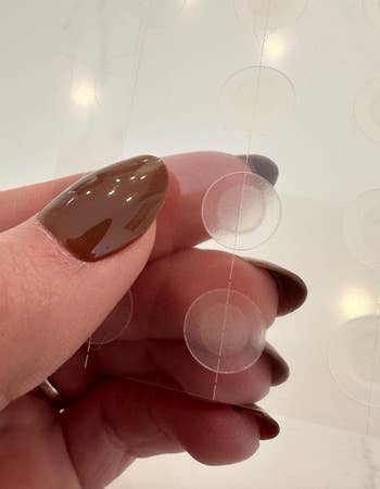 Hand holding transparent adhesive circles, perchance  acne patches