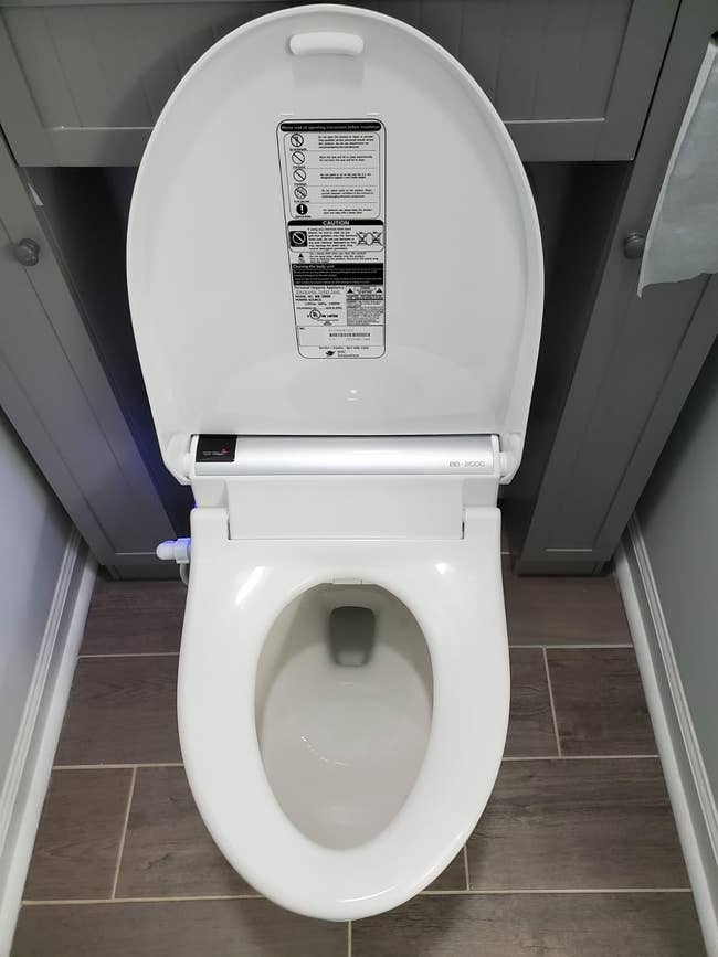A toilet with an attached smart seat and bidet feature and an open lid