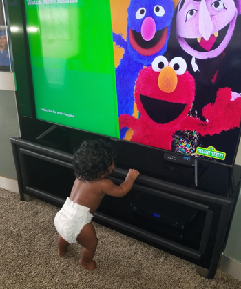reviewer's child watching sesame street and balancing on tv stand with cushion over the edge