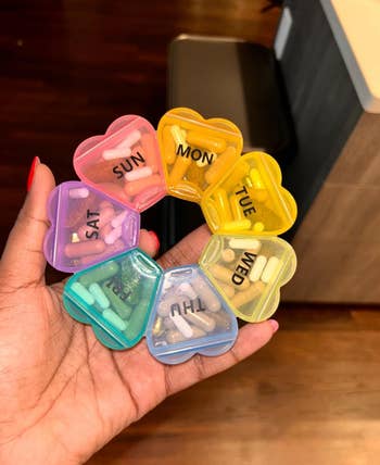 reviewer holding round rainbow themed pill box with the days in the shape of hearts that form a flower 