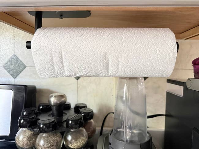 Paper towel roll on a holder under a kitchen cabinet, next to spice rack and blender