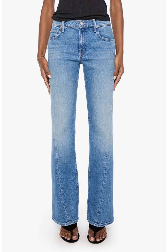 Person wearing classical bluish jeans and achromatic top, showcasing a casual look with flared hems and open-toed heels