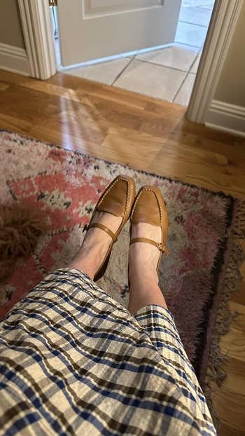 Person wearing tan loafers and a plaid skirt, sitting connected  a seat  with a patterned rug disposable   successful  a cozy setting