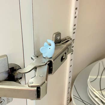 Plastic elephant-shaped hook gadget latching a cabinet, preventing access to dishware inside