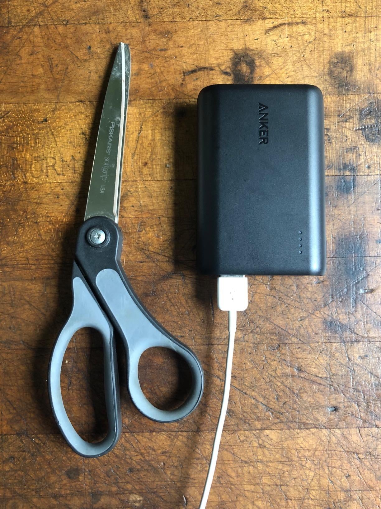 The rectangular portable charger next to a pair of scissors that are larger than it to show its size
