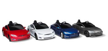 Four Tesla model car toys in red, white, blue, and gray arranged side by side