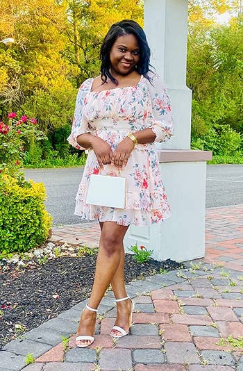 Reviewer wearing white floral thigh-length dress with cinched waist, balloon sleeves, and a ruffled skirt hem outside in white open toe heels