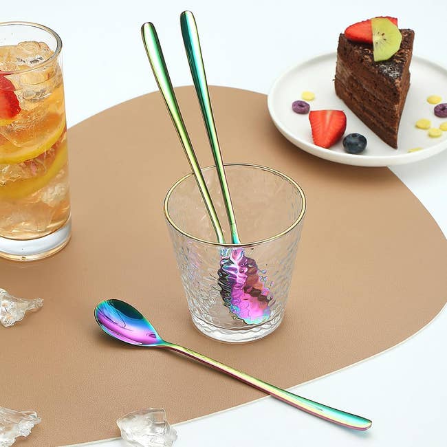 Reusable iridescent metal straw and spoon on a table with a drink and cake slice in the background