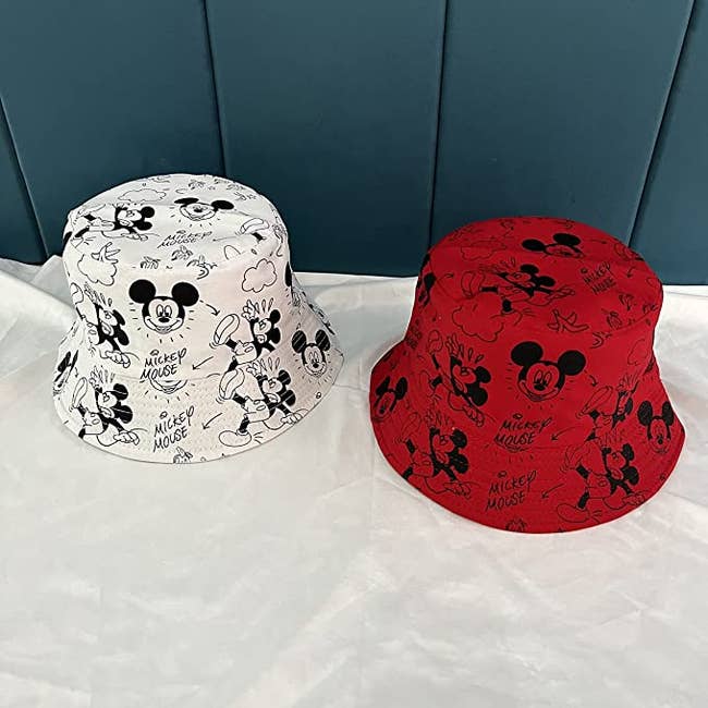 two bucket hats one in cream and one in white with mickey mouse cartoons on them