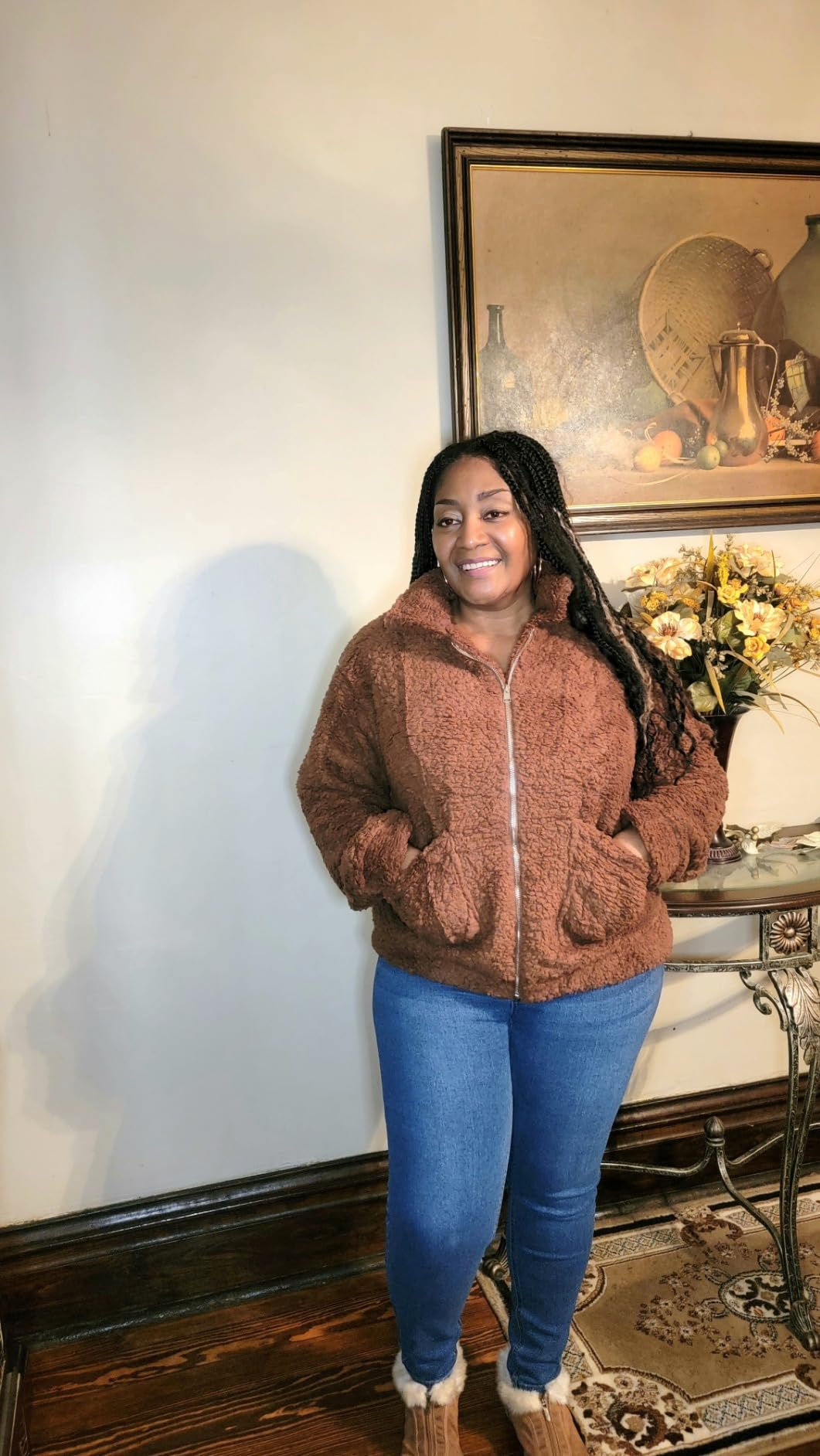 Person successful  casual teddy overgarment  and jeans smiling indoors adjacent   a array  with a decorative floral arrangement
