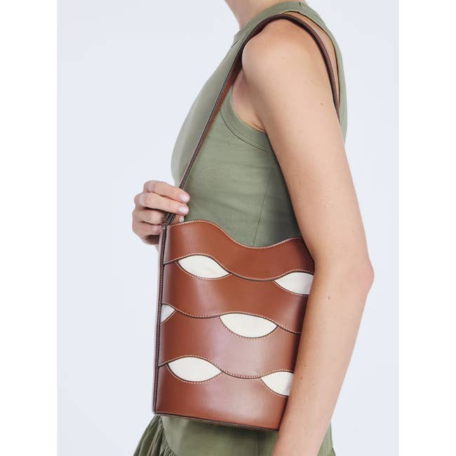 Person holding a stylish brown handbag with wave-shaped accents, wearing a sleeveless top