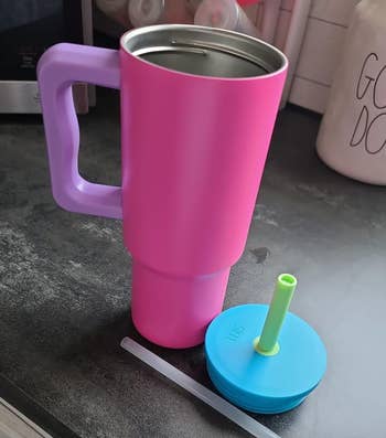 pink tumbler with purple handle and blue lid and green straw 