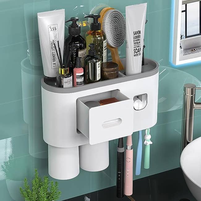 A white and grey toothpaste dispenser with two cups, a drawer, and four toothbrush holders
