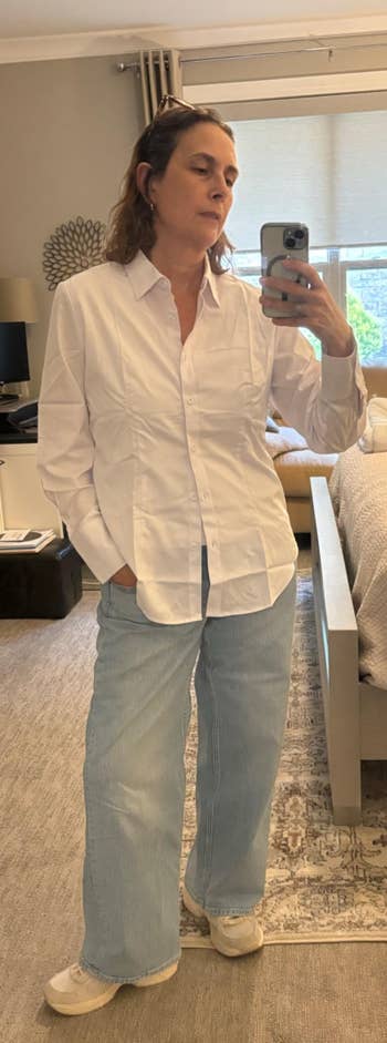 Person taking a selfie successful a chamber mirror, wearing a achromatic button-up shirt, airy jeans, and sneakers