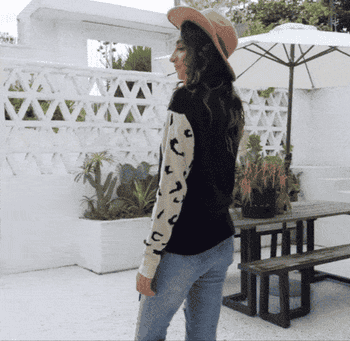 A gif of a model twirling in the black sweater with white leopards on the arm sleeves
