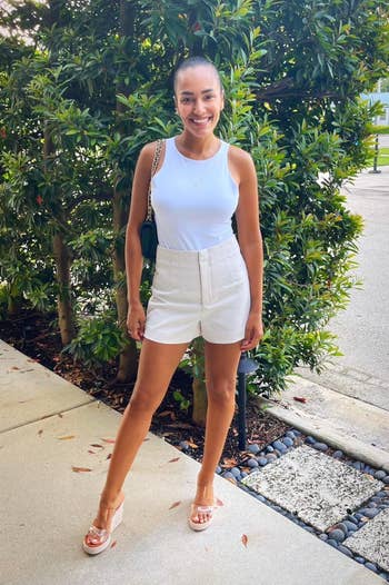 reviewer in a sleeveless white top, high-waisted shorts, and platform sandals