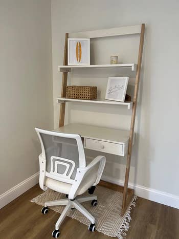 An office chair in front of a leaning shelf with decorative items and a drawer