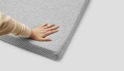 a hand pushing into a gray knit quilt covered mattress topper