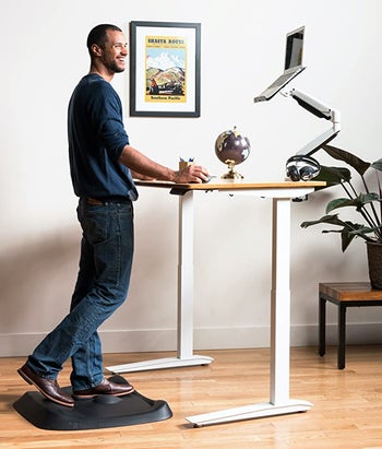 Model standing on a black mat in front of standing desk 