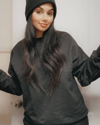 A reviewer wearing a casual sweatshirt and beanie successful  a location  setting, smiling with arms somewhat  raised. Shopping nonfiction  context. Names unknown