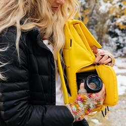 Model putting a camera into the side pocket of the yellow backpack