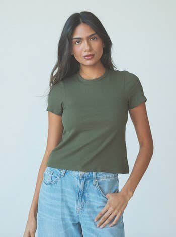 Woman in a plain green t-shirt and blue jeans, standing casually for a shopping ad