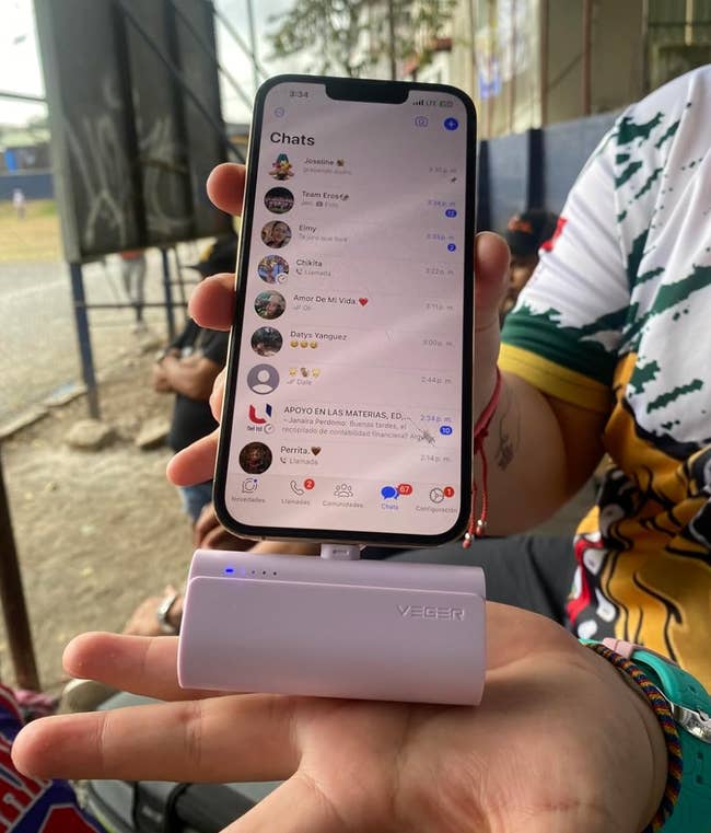 Person holding a smartphone displaying a chat list, with a portable charger attached