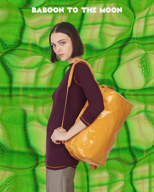 model wearing a bright orange size S duffel bag as a backpack