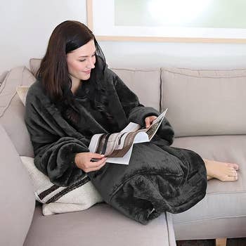 Model laying on the couch while wearing the black blanket hoodie