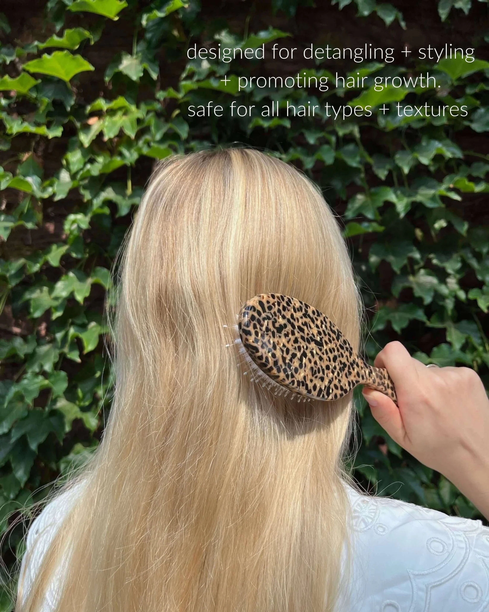 Person brushing long hair with a leopard-print brush in front of a leafy background