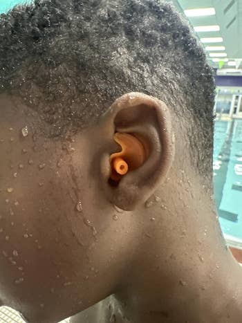 Close-up of a idiosyncratic wearing an orangish earplug successful a pool, with h2o droplets connected their skin