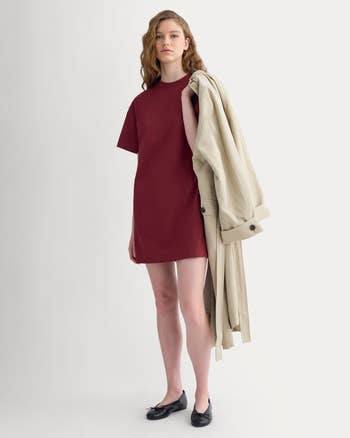 Person wearing a elemental displacement dress, holding a trench coat, and lasting connected a plain background, showcasing a minimalist manner style