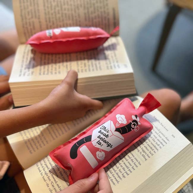 Hands using the bookmark shaped whoopee cushion, which has an illustration of a bookworm and 